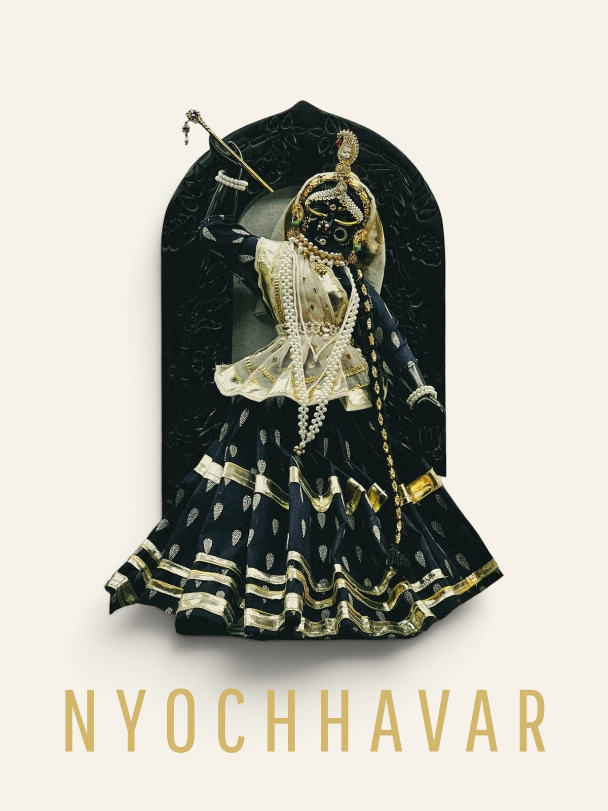 Black marble Shrinathji murti with left arm raised, dressed in navy and gold shringar with carved arch backdrop